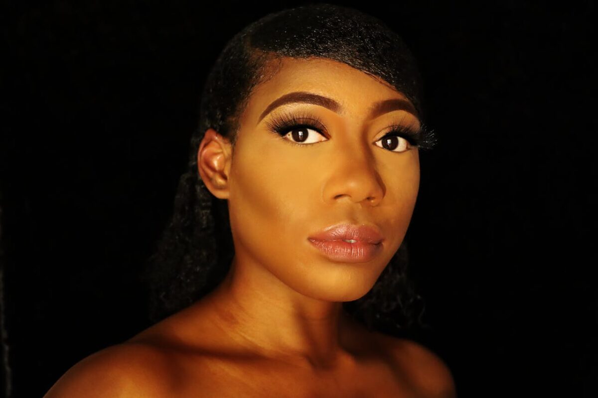 Close-up portrait of a woman showcasing elegant makeup against a black background.