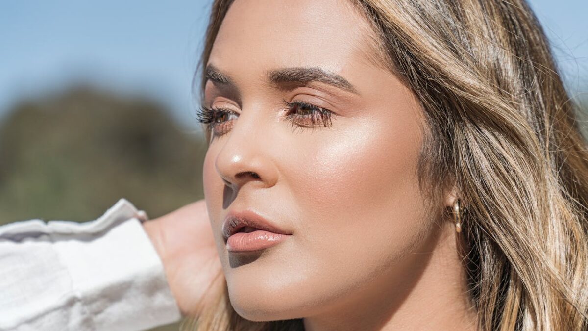 A detailed close-up portrait of a woman with blond hair and flawless skin taken outdoors.